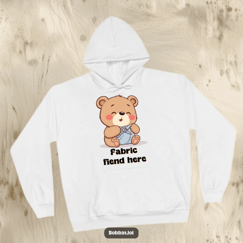 Funny bear giggling while carefully cutting fabric with tiny shears, featured on a warm hoodie.